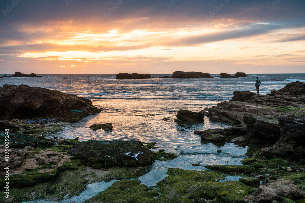 Man standing on a rock and enjoying the sunset on the ocean, Morocco Man standing on a rock and enjoying the sunset on the ocean, Morocco