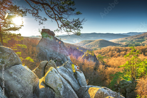 Climber with a beard sitting on a rock looking at the landscape in the highlands surrounded by mountain walls. Forest and hills distant, aspen trees in autumntime photo