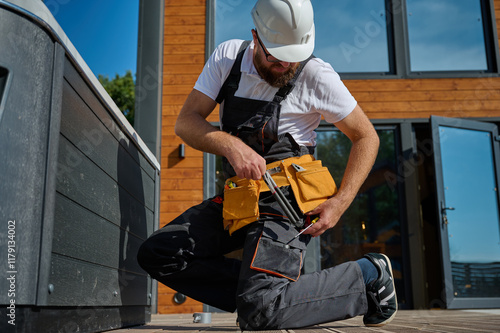 Plumber installing hot tub. Spa technician performing hot tub. Bathtub plumbing. Plumber fixing spa zone. Professional in uniform inspects and prepares a hot tub located on a stylish outdoor patio. photo