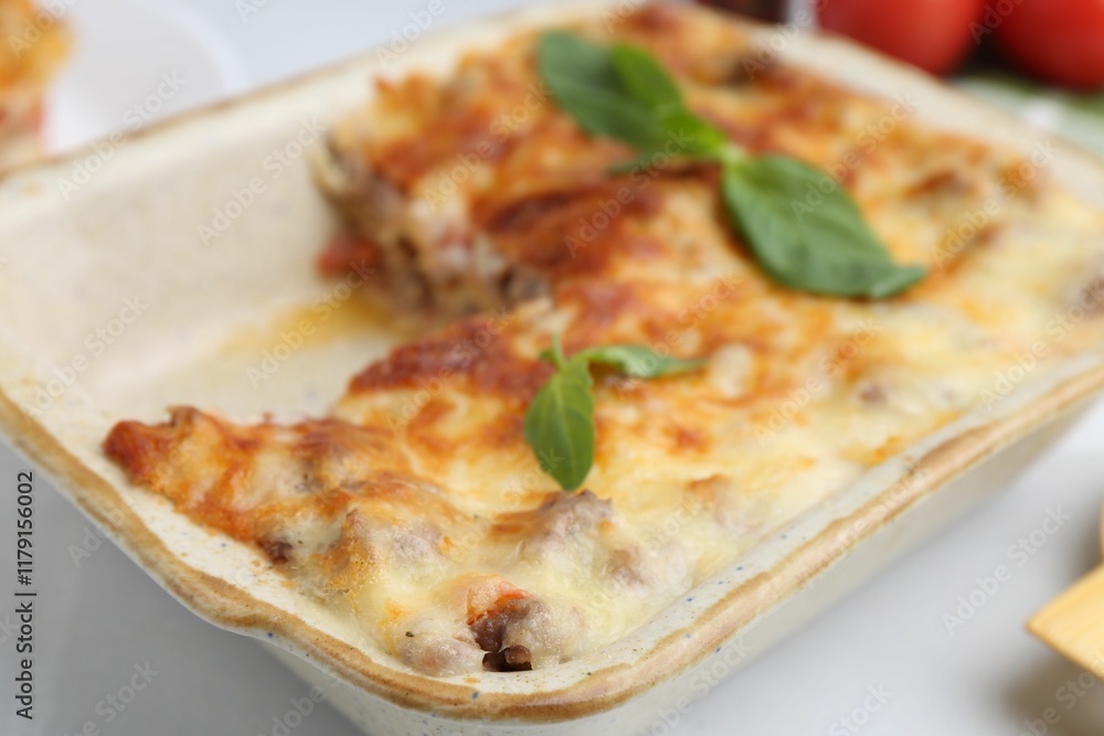 Delicious cooked lasagna with basil in baking dish on white table, closeup Delicious cooked lasagna with basil in baking dish on white table, closeup