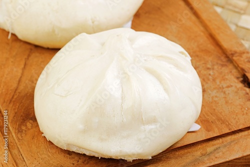 A traditional Chinese steamed bun (baozi) served on a wooden plate, with one bun sliced open revealing its savory meat filling. Soft, fluffy texture with a delicious filling,  photo