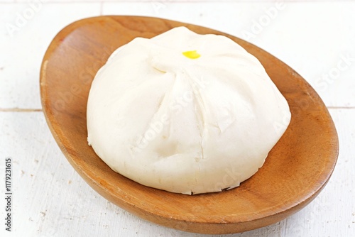 A traditional Chinese steamed bun (baozi) served on a wooden plate, with one bun sliced open revealing its savory meat filling. Soft, fluffy texture with a delicious filling,  photo