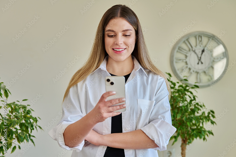 Young smiling woman using smartphone standing at home Young smiling woman using smartphone standing at home