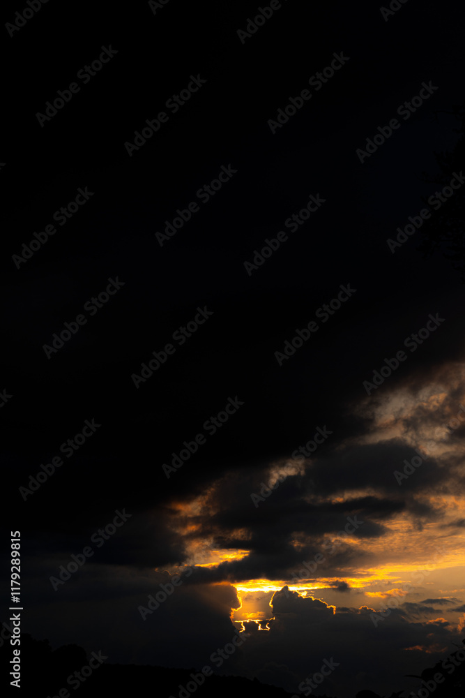 Golden light bursts through dark, heavy clouds during a vibrant sunset, silhouetting the landscape below. Golden light bursts through dark, heavy clouds during a vibrant sunset, silhouetting the landscape below.
