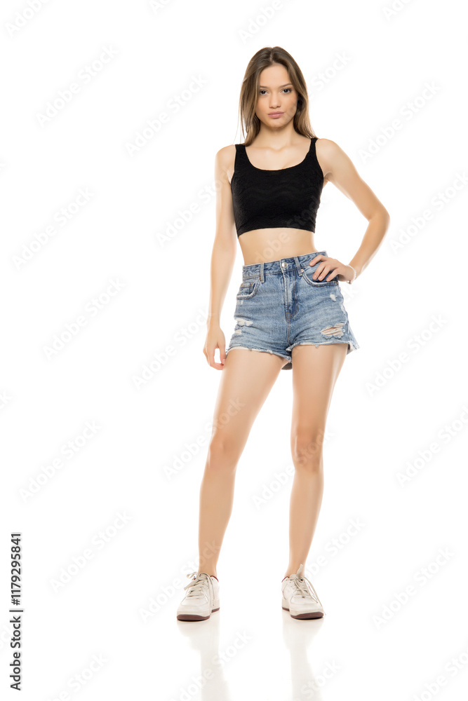 Beautiful young woman in a short blue jeans and black sleeveless shirt on a white studio background. Front view Beautiful young woman in a short blue jeans and black sleeveless shirt on a white studio background. Front view