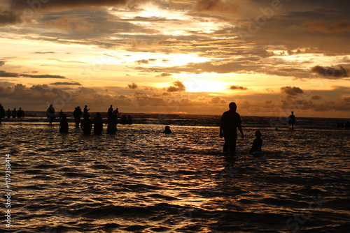 Silhouette people man a woman on the sunset background, mSunset on the tropical beach Seminyak. The tourists watching for beautiful sunset in the sea. Coast of the sea at colorful sunset. photo