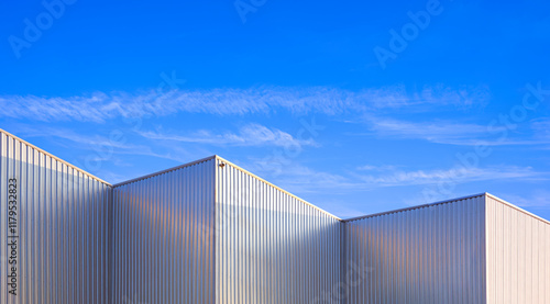 Factory warehouse industry building with geometric metal corrugated steel wall and rooftop against blue sky background, Modern industrial exterior architecture backdrop design in minimal style