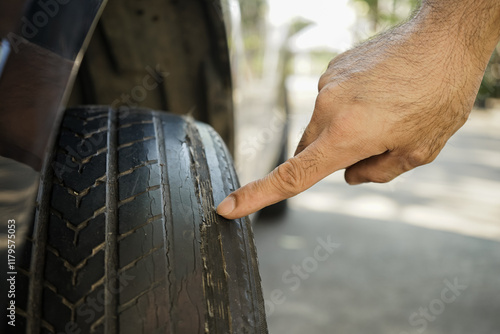 close up of hand points at a worn tire with bald tread. Concept of car maintenance and dangers from old and worn tires from use