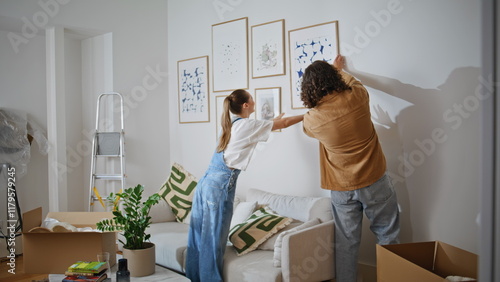Couple hanging pictures wall apartment. Happy woman and man enjoy collaborating 