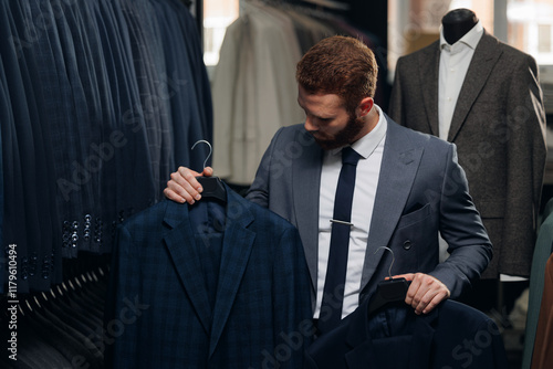 Handsome professional tailor man offers two suits to choose in menswear store. Luxury designer atelier of suit photo