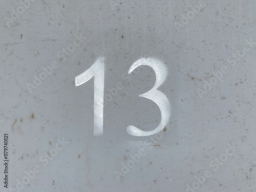 White number 13 on aged gray background. Thirteen on textured surface photo