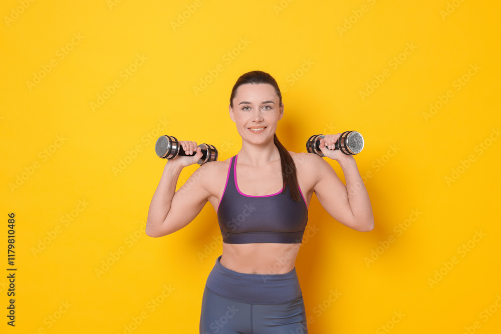 Smiling woman with dumbbells training on yellow background Smiling woman with dumbbells training on yellow background