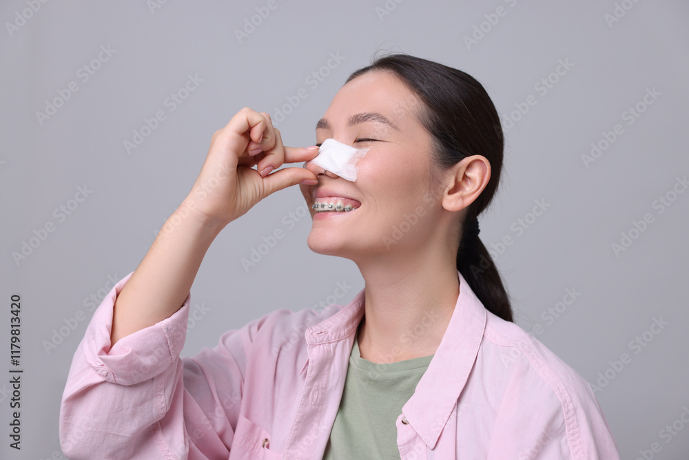 Woman with medical bandage on her nose after plastic surgery operation against light grey background