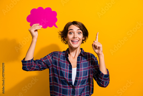 Portrait of impressed smart girl with bob hairstyle wear checkered shirt hold dialog bubble have idea isolated on yellow color background photo