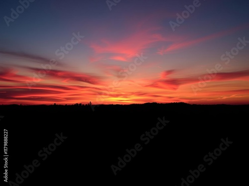 Mountain landscape with vibrant orange and pink skies as the sun sets behind towering peaks, sunset, clouds, silhouette photo