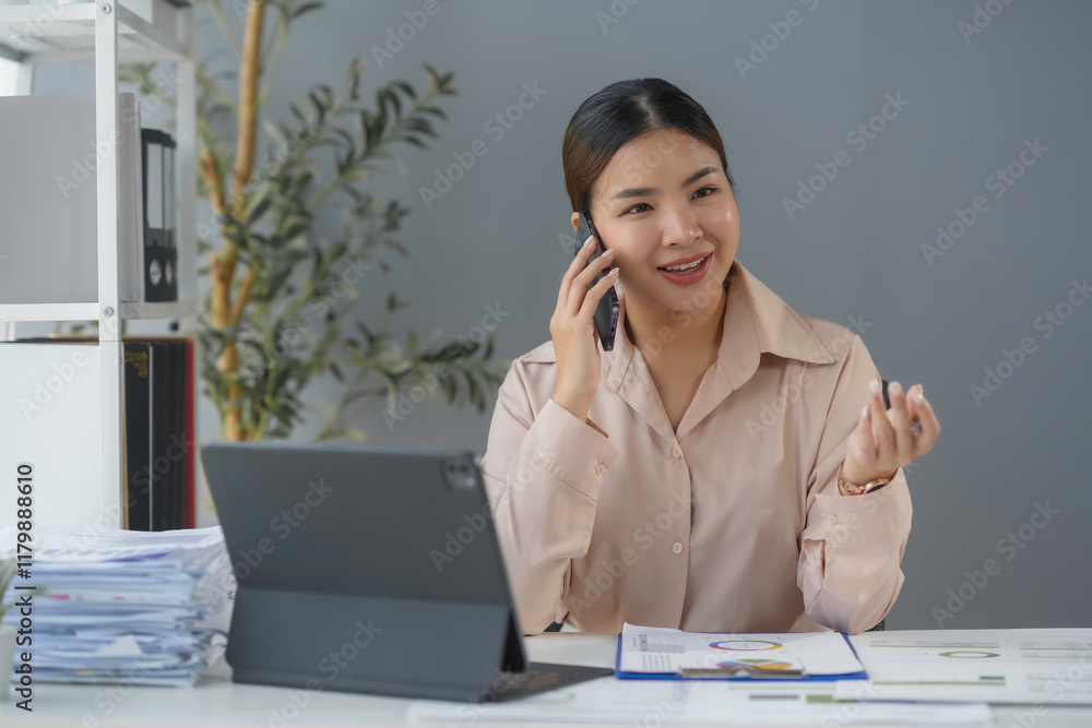 Young businesswoman smiling and talking on phone while working with financial documents and digital tablet in modern office Young businesswoman smiling and talking on phone while working with financial documents and digital tablet in modern office