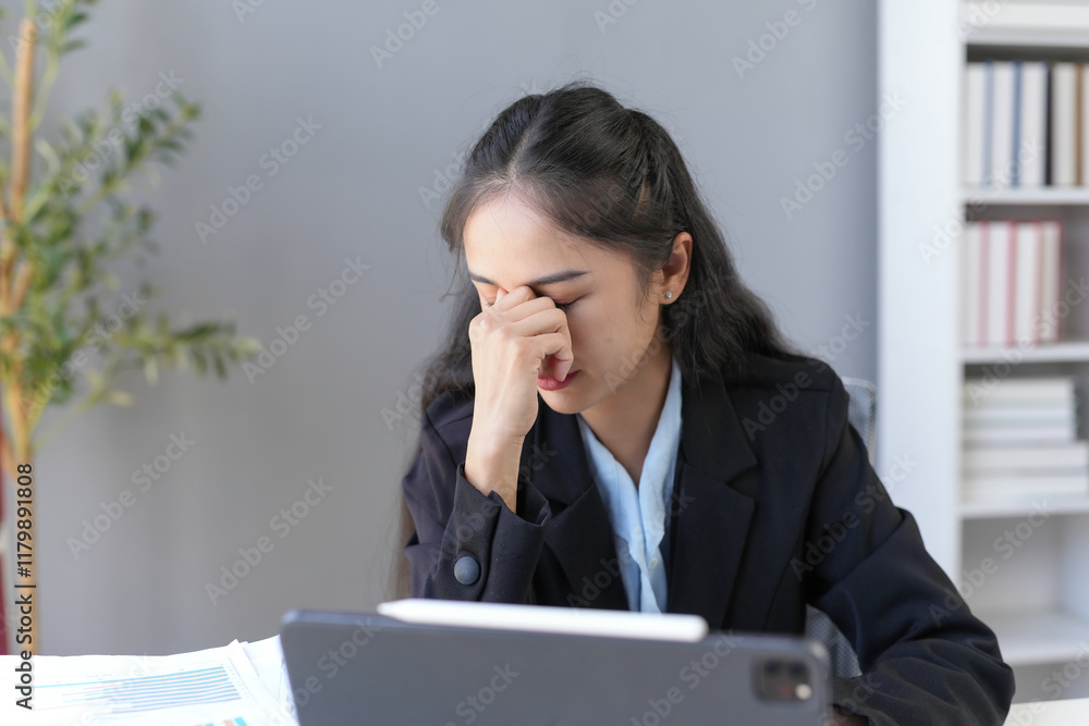 Young businesswoman suffering from headache, massaging her nose and eyes, feeling tired from work in office Young businesswoman suffering from headache, massaging her nose and eyes, feeling tired from work in office