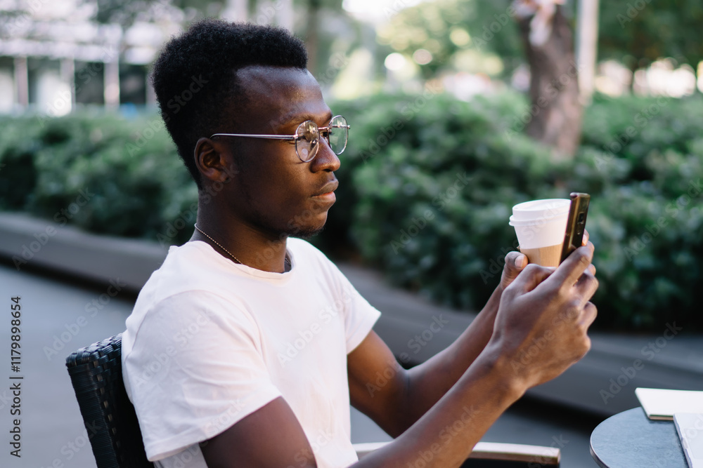 Black man with coffee browsing smartphone in street cafe Black man with coffee browsing smartphone in street cafe