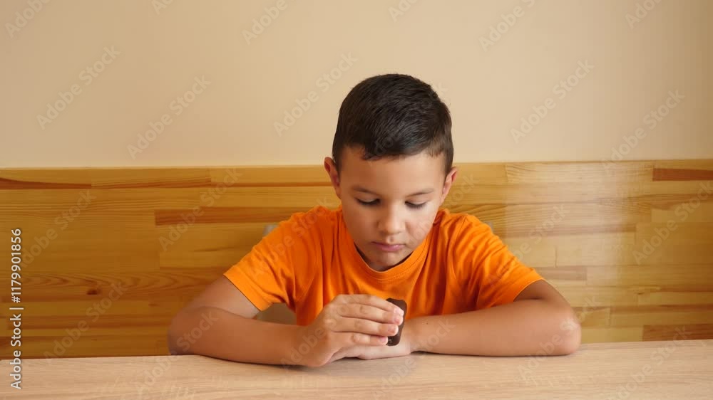The boy is eating chocolate while sitting at the table. The boy is eating chocolate while sitting at the table.
