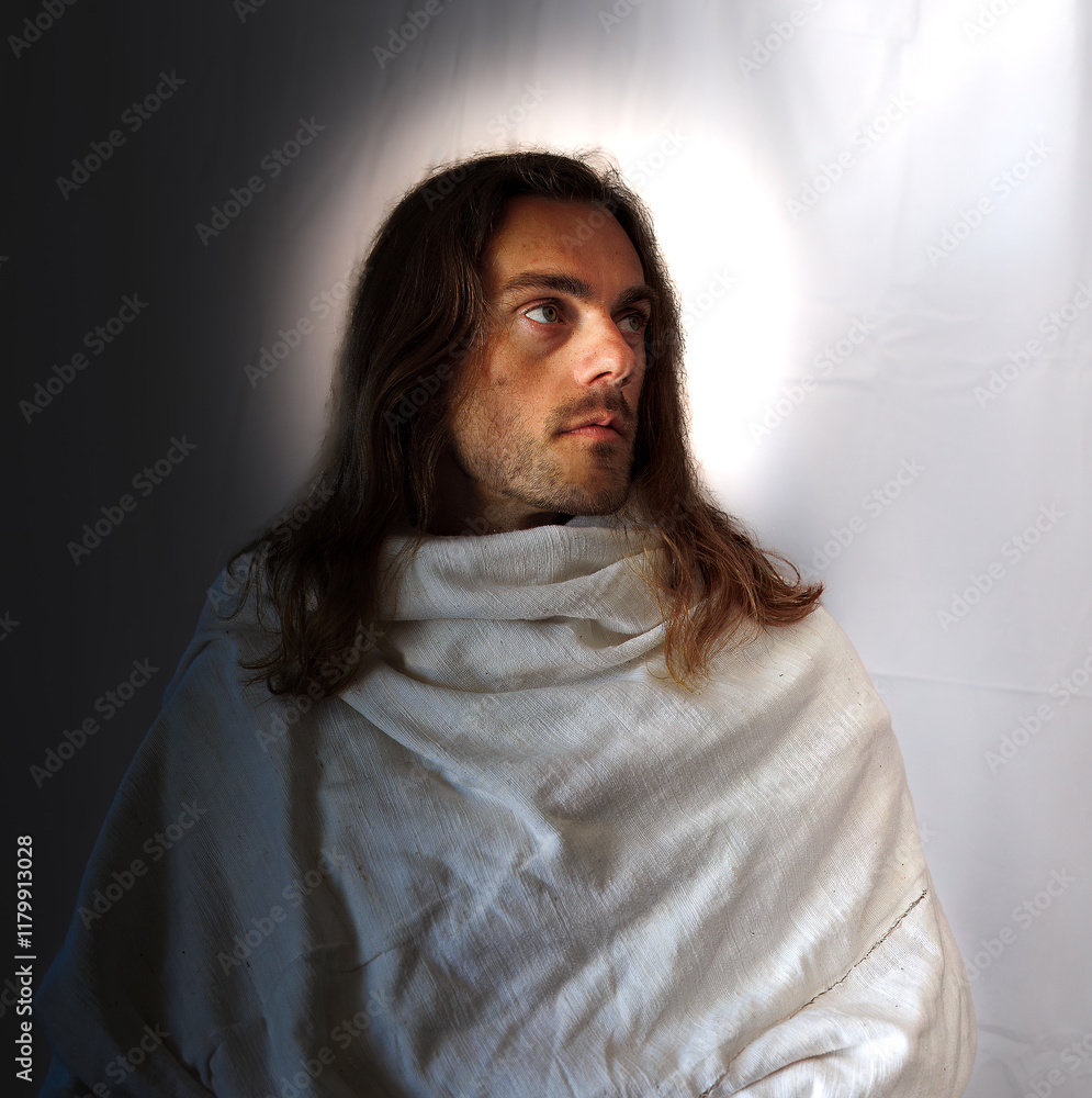 Portrait of a man with a halo, resembling Jesus Christ or holy man. He is looking upwards, dressed in a white robe and has long hair and a beard.