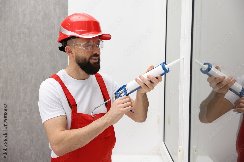 Worker with caulking gun sealing window indoors Worker with caulking gun sealing window indoors