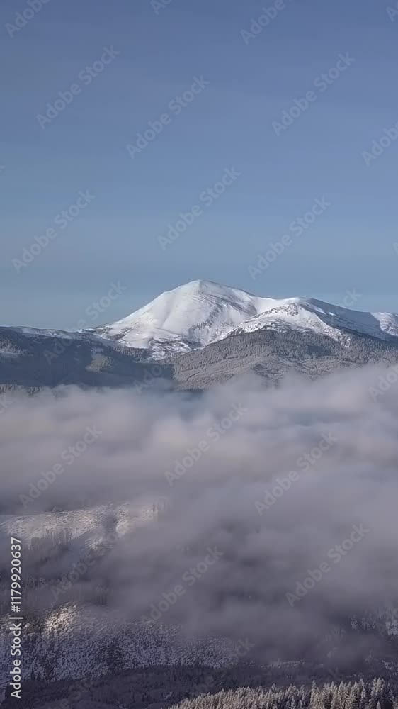 Snow-covered mountain peaks rise majestically above a blanket of clouds during early morning, showcasing stunning natural beauty and the tranquility of the wilderness. Vertical footage Snow-covered mountain peaks rise majestically above a blanket of clouds during early morning, showcasing stunning natural beauty and the tranquility of the wilderness. Vertical footage