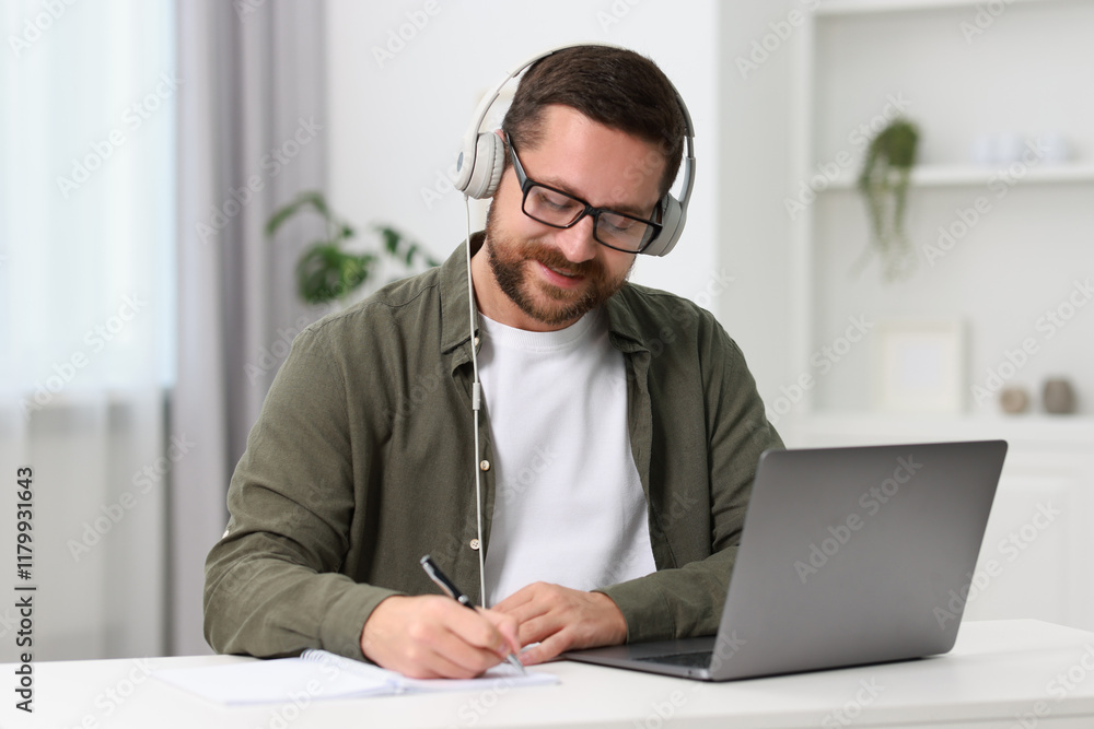 Interpreter in headphones taking notes while having video chat via laptop at white table indoors Interpreter in headphones taking notes while having video chat via laptop at white table indoors
