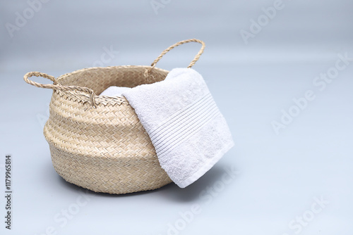 Straw wicker basket and white natural cotton towel on gray background. Fashionable bamboo basket stylish interior item eco design handmade, copyspace