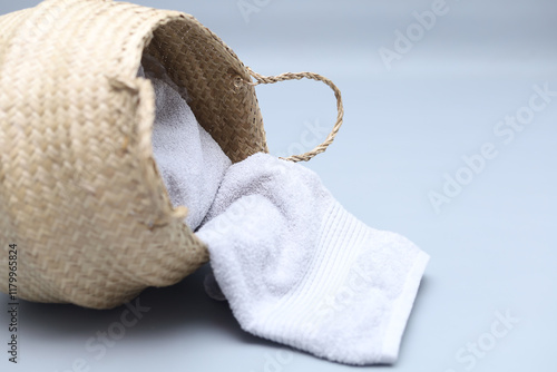Straw wicker basket and white natural cotton towel laying on gray background. Fashionable bamboo basket. Eco friendly and zero waste item.