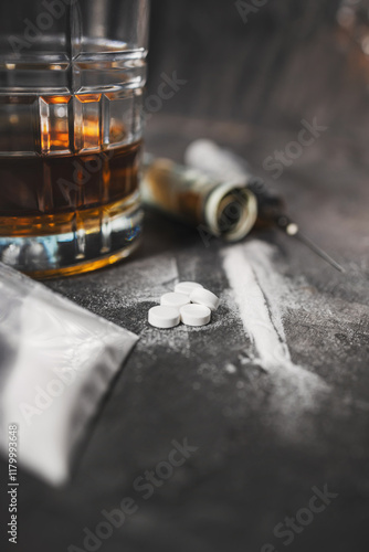 Fotografia White narcotic pills, an alcoholic drink in a glass, a syringe with a dose of heroin, a line of cocaine powder and US dollar bills on a dark background