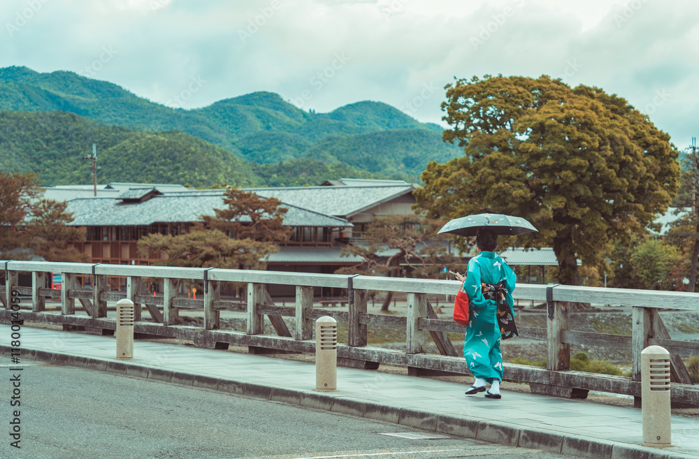 Fototapeta premium Picturesque scene with a woman holding an umbrella and wearing a traditional japanese kimono on the Togetsukyo Bridge in Arashiyama, Kyoto.