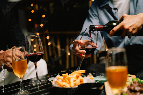 Fotografía Nightcap Rendezvous: Pouring red wine into a glass during a cozy evening gathering with friends, enjoying drinks and appetizers