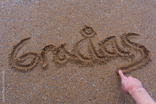 Handwriting 'Gracias' in the sand with a hand finishing the word photo