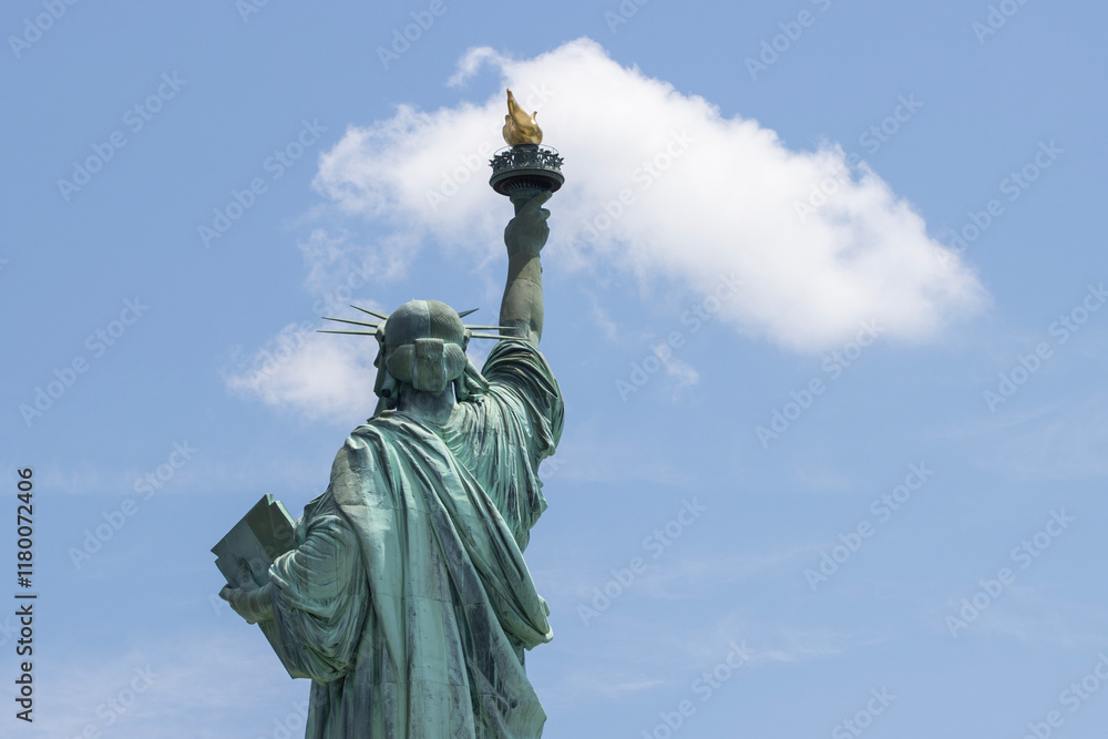 Fototapeta premium Rear view of the Statue of Liberty on the Liberty Island in New York against a blue sky and clouds.