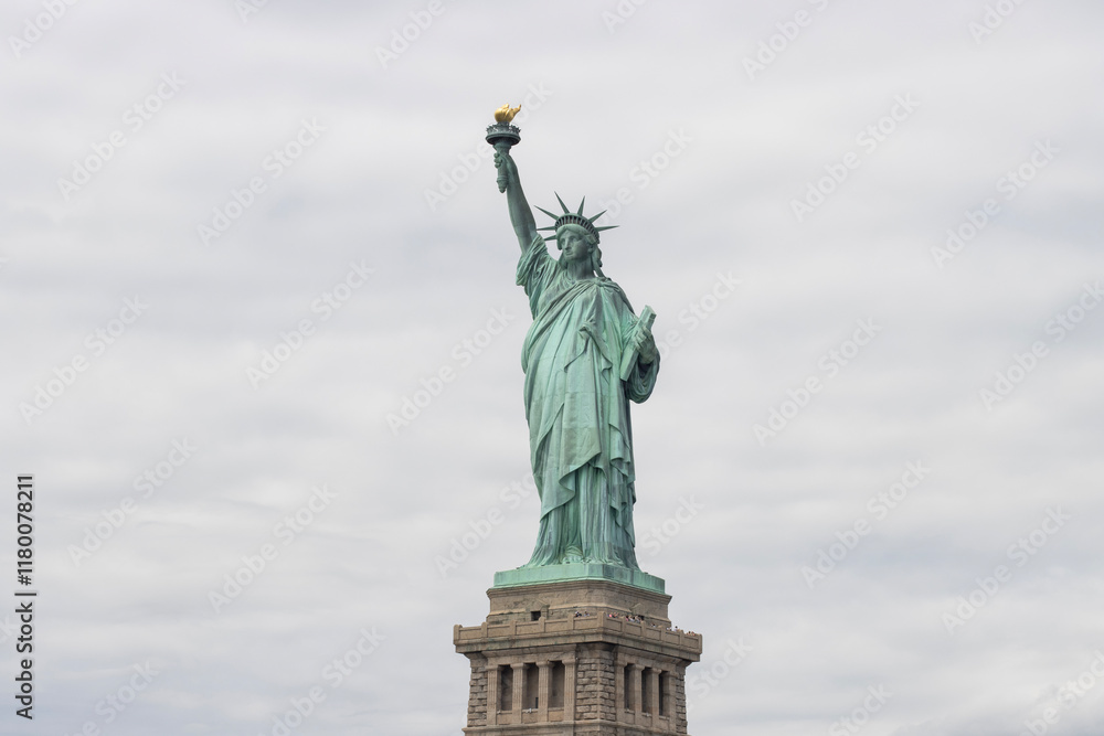 Fototapeta premium The Statue of Liberty standing on a pedestal on the Liberty Island in New York against a cloudy sky.