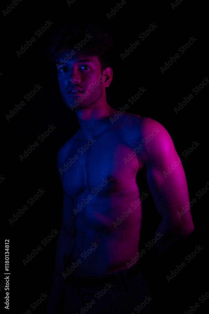 Fototapeta premium Junger Mann aus Indien steht mit freiem Oberkörper in buntem Licht und posiert