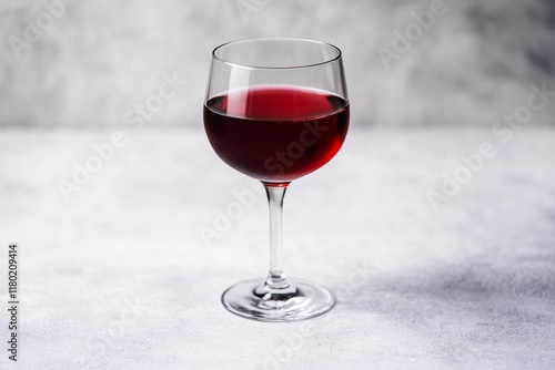 A crystal clear glass filled with deep red wine sits elegantly on a smooth light gray surface, highlighting a sophisticated ambiance perfect for unwinding after a long day photo