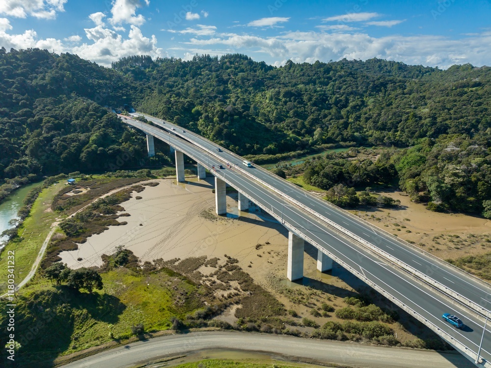 Fototapeta premium Aerial view of a highway bridge over a dried-up riverbed. Traffic flows smoothly across the modern concrete structure. Johnstones Hill Tunnels , Waiwera, Auckland, New Zealand