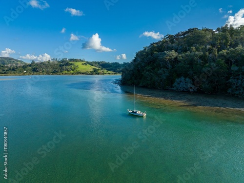 Tranquil sailboat on a Puhoi River, surrounded by lush green hills and a clear blue sky. Peaceful scene. Wenderholm Regional Park, Waiwera, Auckland, New Zealand photo