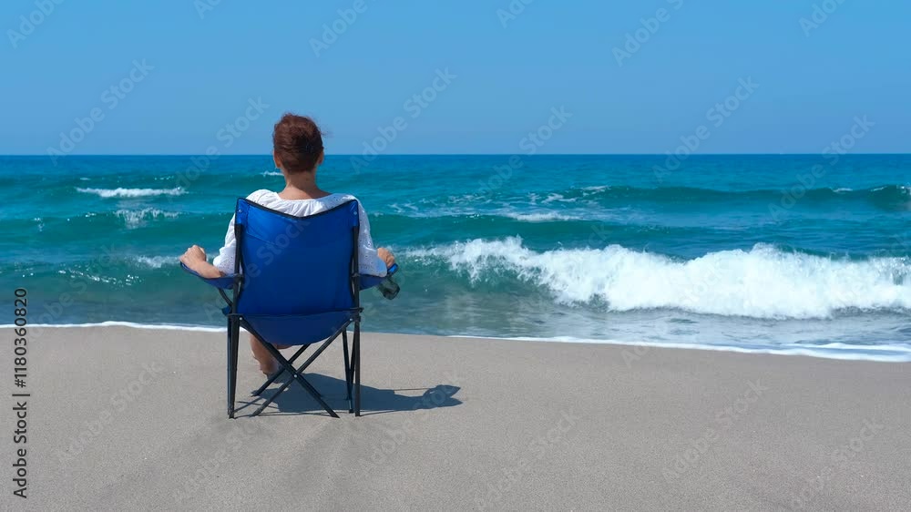 Enjoy the waves alone. Woman is enjoying a peaceful moment on the beach, sitting on a chair and contemplating the ocean waves crashing on the shore Enjoy the waves alone. Woman is enjoying a peaceful moment on the beach, sitting on a chair and contemplating the ocean waves crashing on the shore