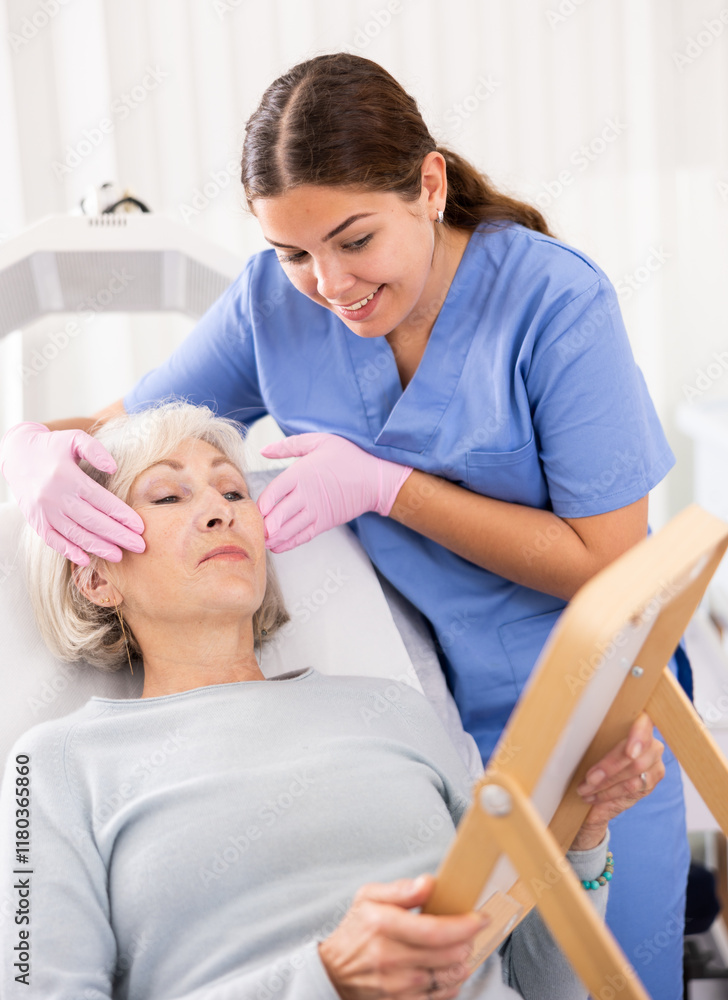 Obraz premium Pleasant young woman doctor consulting aged woman patient lying on clinical chair about face aesthetic