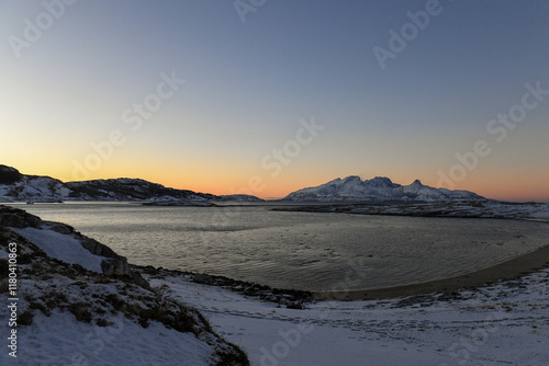 Landscape shot highlighting the rugged mountains and snow-covered beaches of arctic norway during a brief golden hour during the long winters. photo