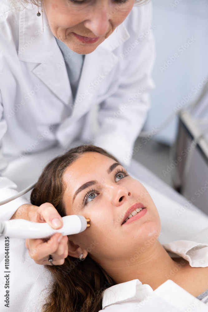 Mature female dermatologist performing cosmetology procedure for young woman, RF lifting and vacuum massage for facial skin therapy in clinic Mature female dermatologist performing cosmetology procedure for young woman, RF lifting and vacuum massage for facial skin therapy in clinic
