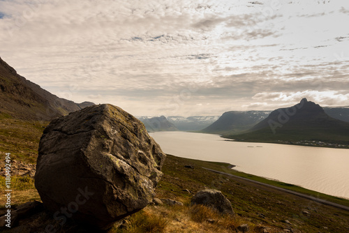 A large rock sits atop a hill overlooking a Fjord in the westfjords. Iceland