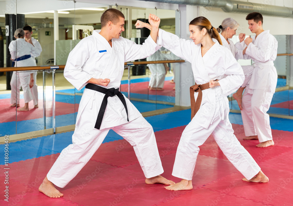 Caucasian man and woman in kimono sparring during group karate training. Senior woman and teenage boy fighting in background. Caucasian man and woman in kimono sparring during group karate training. Senior woman and teenage boy fighting in background.