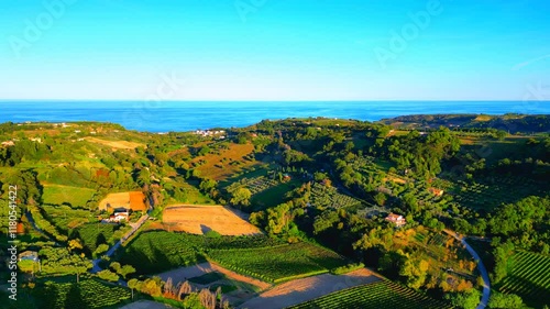 Smooth aerial push-in shot from Campofilone, swathes of green and brown fields lie on the Marche valleys and hills between roads, buildings, thrifty trees, vegetation, advancing into the Adriatic Sea photo