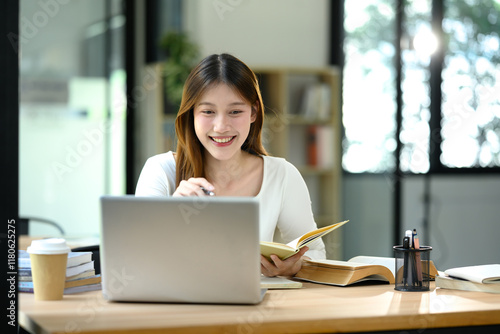Free Download Cheerful young woman using laptop in a bright and modern study space - GFXLoad