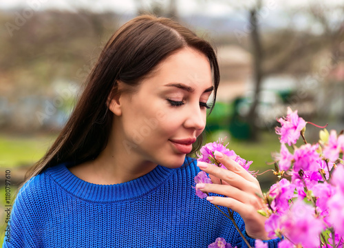 Russian woman in a blue sweater smelling pink rhododendron flowers in Primorsky Krai, Russia. The scene captures the essence of springtime and natural beauty photo