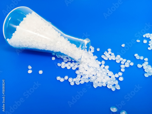 Virgin polymer granules with blue background, virgin homopolymer resin raw material poured from glass with blue background, suitable for plastic company profile product catalog design photo