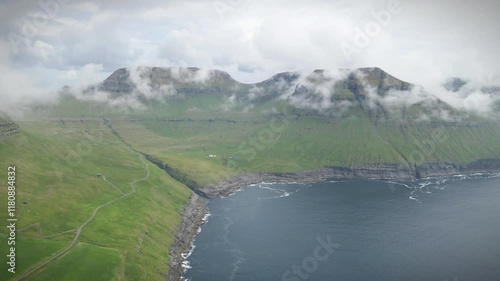 Wallpaper Mural Drone shot of low clouds covering the green mountains of Norðradalur, a village located on the island of Streymoy in the Faroe Islands, with a winding road and a rocky coastline Torontodigital.ca